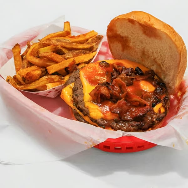 Double cheeseburger with bacon and barbecue sauce, served with a side of fries in a red basket.