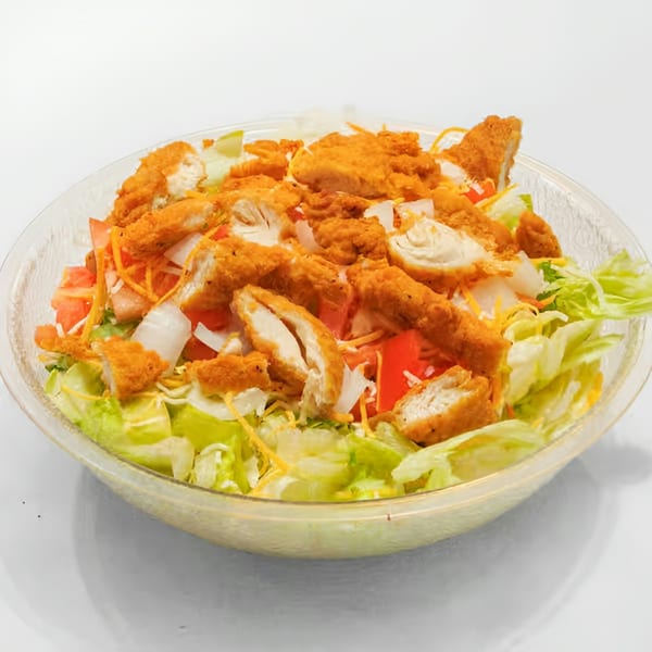 Crispy chicken salad with lettuce, tomatoes, onions, and shredded cheese in a clear bowl.
