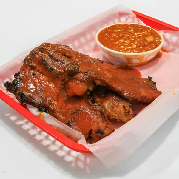 Saucy BBQ ribs with a side of baked beans in a red basket lined with white paper.