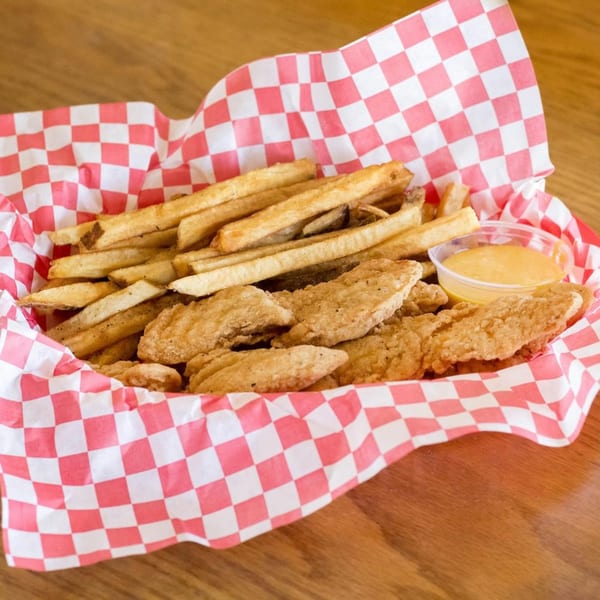 Chicken tenders and french fries in a red and white checkered paper-lined basket with dipping sauce.