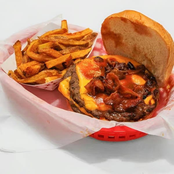 A juicy cheeseburger with bacon and sauce, served with a side of golden fries in a red basket.
