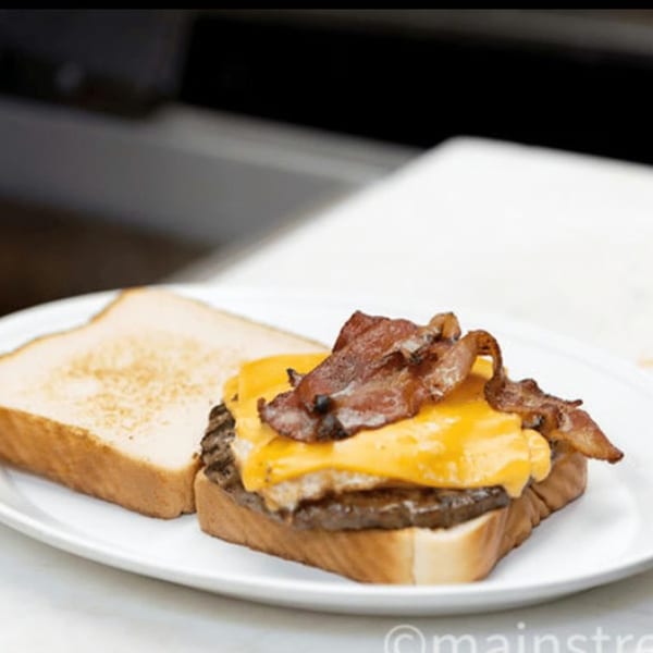 A patty melt with melted cheese and bacon on toasted bread, served on a white plate.