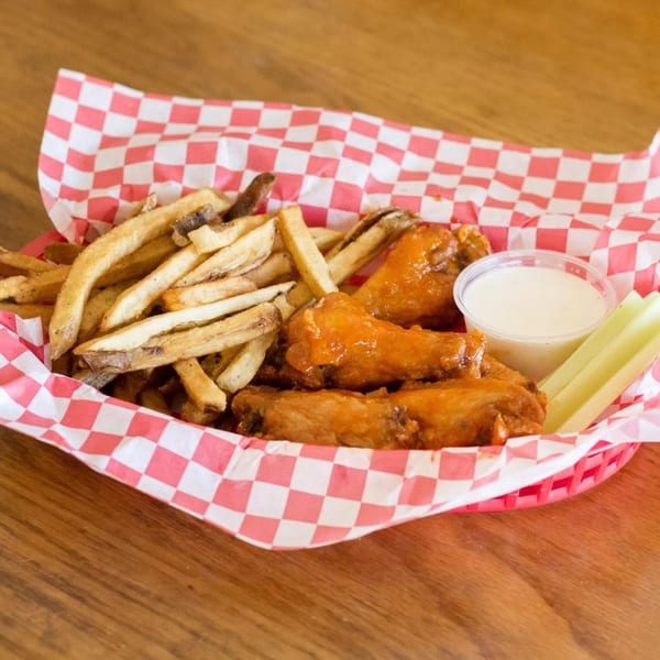 A red and white checkered basket filled with crispy french fries, buffalo wings, ranch, and celery sticks.