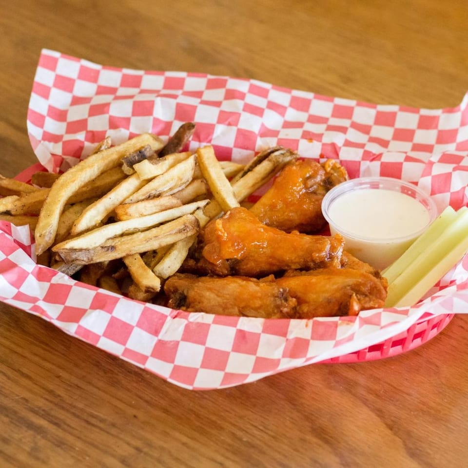 A red and white checkered basket filled with crispy french fries, buffalo wings, ranch, and celery sticks.