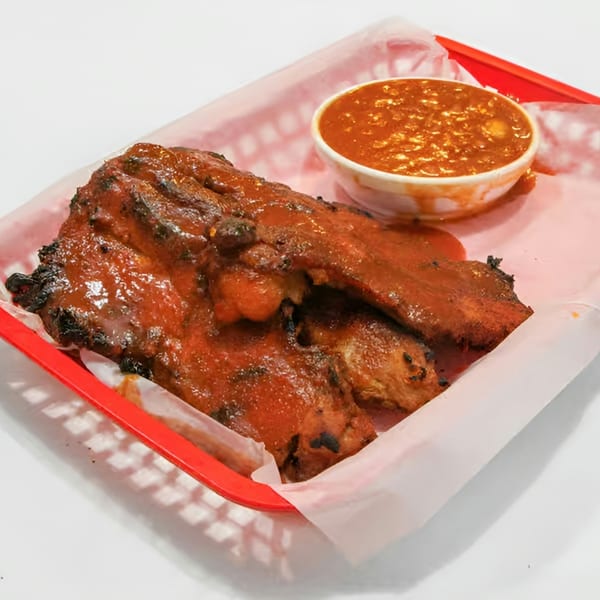 Barbecue ribs covered in sauce, served in a red basket with a side of baked beans.