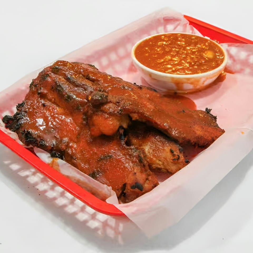 Barbecue ribs covered in sauce, served in a red basket with a side of baked beans.