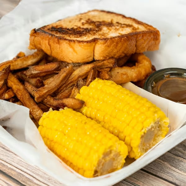 A grilled cheese sandwich, fries, two corn on the cob halves, and a dipping sauce.