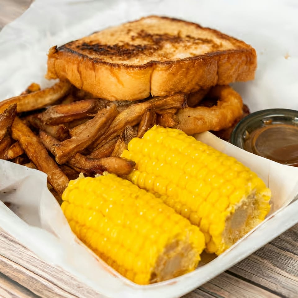 A grilled cheese sandwich, fries, two corn on the cob halves, and a dipping sauce.