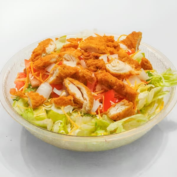 Crispy chicken salad with lettuce, tomatoes, onions, and shredded cheese in a clear bowl.