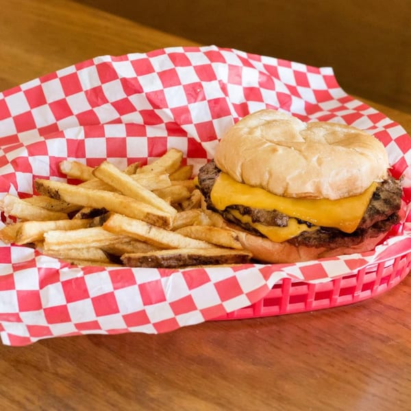 Cheeseburger with two patties and fries in a red and white checkered basket on a wooden table.