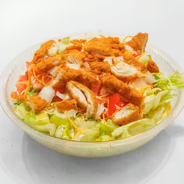 Crispy chicken salad with lettuce, tomatoes, onions, and shredded cheese in a clear bowl.