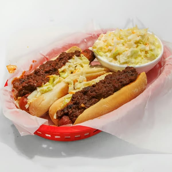 Two chili dogs with coleslaw in a red basket, with a side of coleslaw.