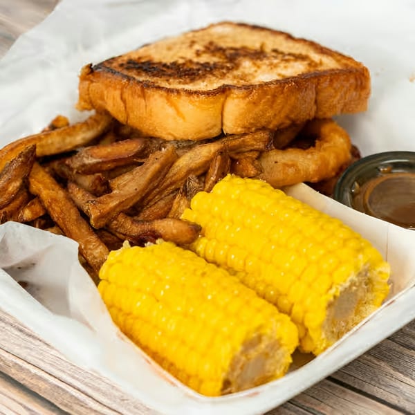 A fried chicken sandwich, fries, onion rings, corn on the cob, and dipping sauce in a paper tray.